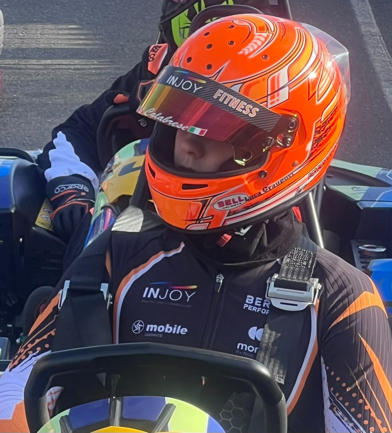Nahaufnahme von Luca Graupner mit orangem Helm, Partnerlogos auf dem Rennanzug